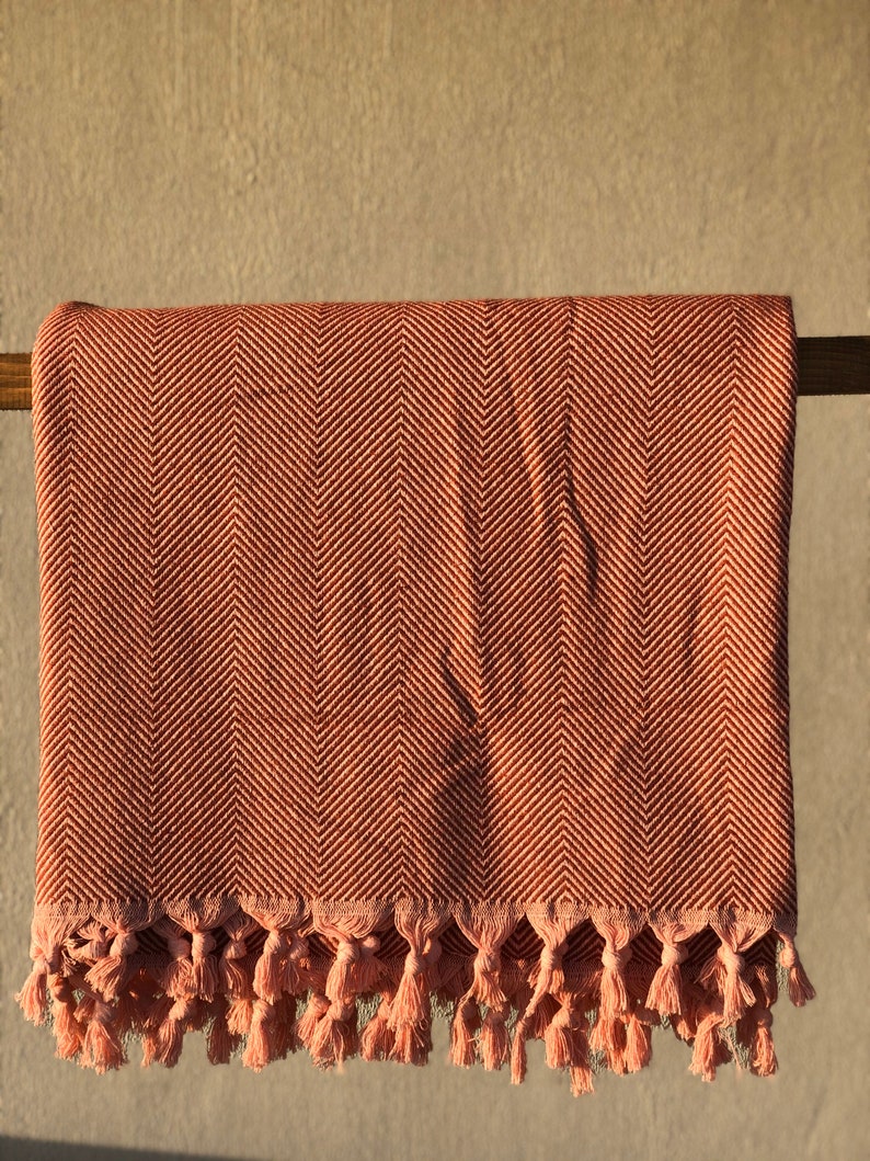 May include: A pink and brown herringbone throw blanket with a fringe border. The blanket is draped over a wooden rod.