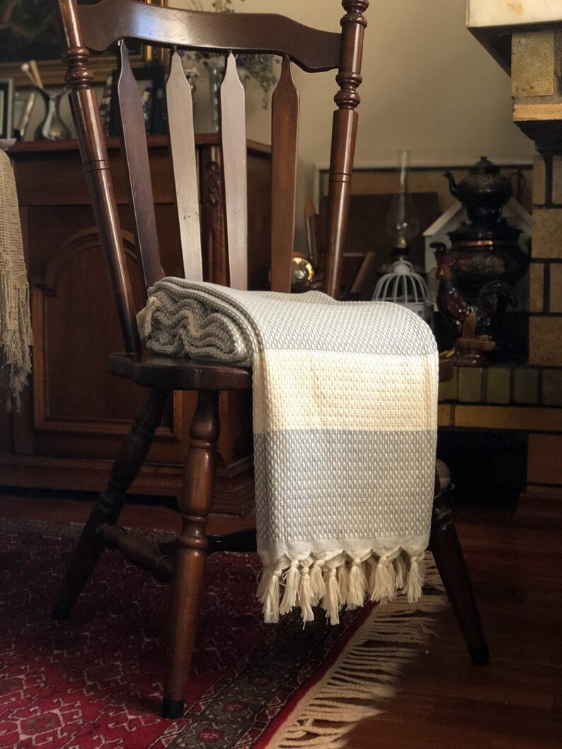 May include: A light blue and white striped throw blanket with fringe on a wooden chair. The blanket is folded and draped over the back of the chair.