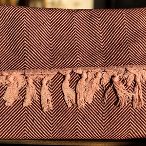 May include: A burgundy and pink throw blanket with a herringbone pattern and a fringe border.