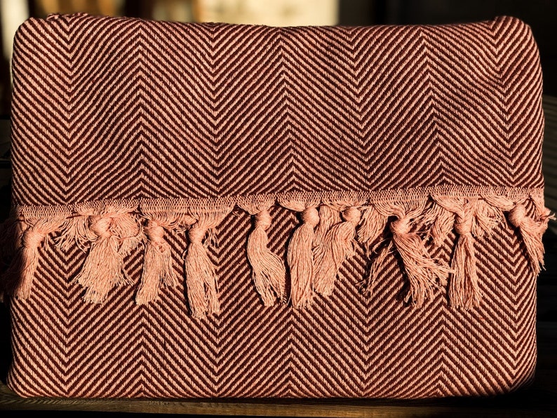 May include: A burgundy and pink throw blanket with a herringbone pattern and a fringe border.