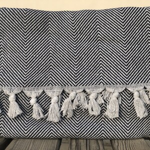 May include: Black and white chevron patterned throw blanket with a fringe border. The blanket has a subtle sheen and is made of a soft, woven fabric.