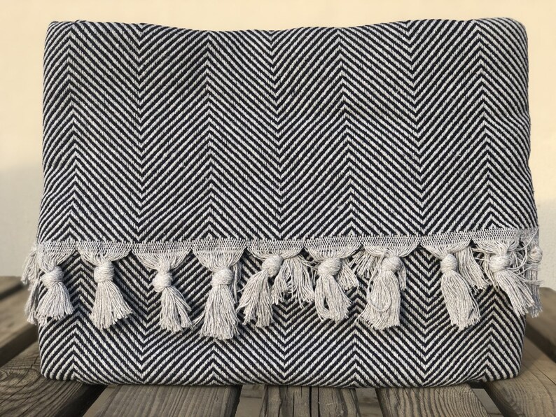 May include: Black and white chevron patterned throw blanket with a fringe border. The blanket has a subtle sheen and is made of a soft, woven fabric.