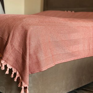May include: A red and white chevron patterned throw blanket with tassels on a bed.