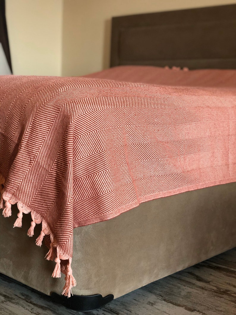 May include: A red and white chevron patterned throw blanket with tassels on a bed.