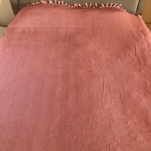 May include: A pink and white herringbone patterned throw blanket with fringe on the edges.