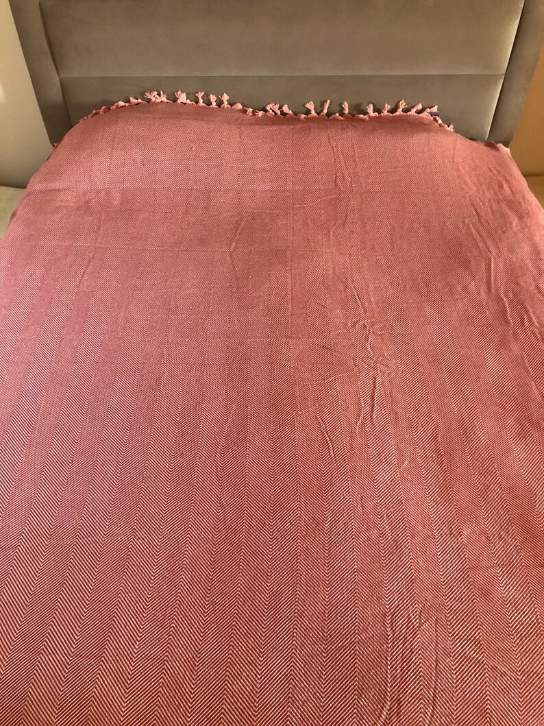May include: A pink and white herringbone patterned throw blanket with fringe on the edges.