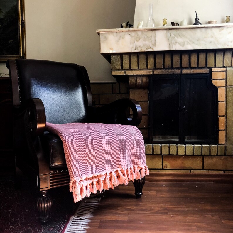 May include: A dark brown leather armchair with a pink and white throw blanket. The armchair is in front of a brick fireplace with a black metal grate.