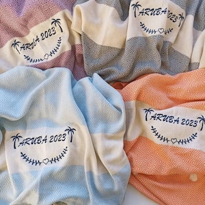 May include: Four beach towels with a striped pattern in different colors. Each towel has the text "ARUBA 2023" embroidered in blue with palm trees and a heart.