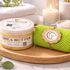 May include: A wooden tray holds a jar of shea butter and a green mesh washcloth. The shea butter jar has a white lid and a label that reads "Shea Butter 100% Natural & Organic". A tag on the washcloth reads "My Organic Spa".