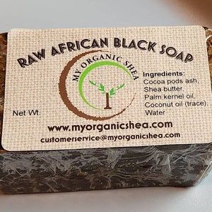 May include: A bar of raw African black soap wrapped in plastic. The label reads "Raw African Black Soap My Organic Shea" and lists the ingredients: Cocoa pods ash, Shea butter, Palm kernel oil, Coconut oil (trace), Water. The website address is www.myorganicshea.com and the customer service email is customerservice@myorganicshea.com.