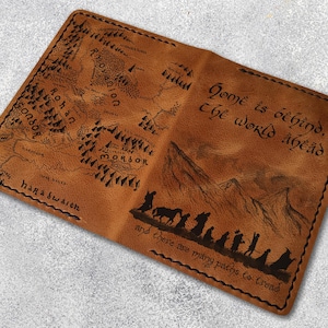 May include: A brown leather wallet featuring a map and text from a fantasy novel. The wallet has a stitched border and includes the phrases "Home is behind, the world ahead" and "and there are many paths to tread."