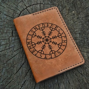 May include: A brown leather passport holder with a black Vegvisir symbol and runes around the edge.