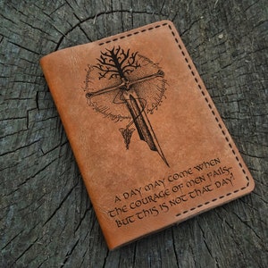 May include: A brown leather passport cover with an engraved design of a tree, a sword, and a quote: "A day may come when the courage of men fails, but this is not that day!"