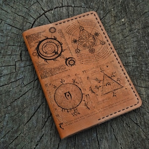 Könnte beinhalten: Ein braunes Lederjournal mit einem genähten Rand und einem Design aus verschiedenen geometrischen Symbolen und Mustern, die in die Abdeckung gebrannt sind.