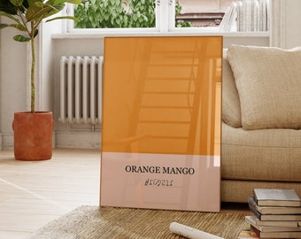 May include: A large, rectangular, orange-colored poster with the text "ORANGE MANGO #f09211" printed on it. The poster is leaning against a beige couch in a room with a large window and a potted plant.