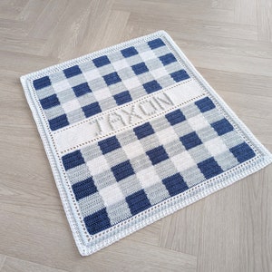 May include: A blue and white crocheted baby blanket with a gingham pattern and the name "Jaxon" embroidered in white.