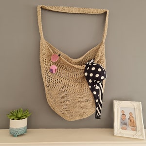 May include: A beige crocheted tote bag hanging on a gray wall. The bag has a black and white polka dot fabric inside. There is a small potted succulent plant on a white shelf below the bag.