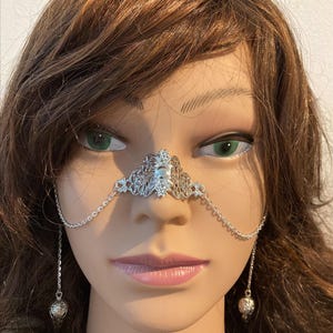 May include: A silver nose chain with a decorative filigree design and dangling ball charms.