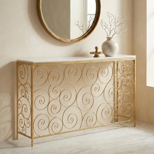 Può includere: Un tavolo console rettangolare con piano in marmo bianco e base in metallo dorato caratterizzata da un intricato motivo di spirali circolari interconnesse. Il tavolo è posizionato contro una parete con uno specchio rotondo con cornice dorata.