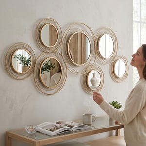 Peut inclure: Un ensemble décoratif mural composé de six miroirs circulaires, chacun encadré par des anneaux en fil métallique doré concentriques de tailles variées. Les miroirs sont disposés en groupe et présentent des surfaces en verre réfléchissant.