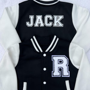 May include: Black and white varsity jacket with white sleeves and a black body. The back of the jacket has the name "JACK" in white letters. The front of the jacket has a white letter "R" on the right side.