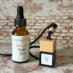 May include: A brown glass bottle with a black dropper and a label that reads "Noir J25". Next to it is a wooden block and a small black bottle, both labeled "Noir J25". The items are connected by a black cord.