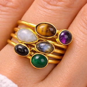Anillos apilables dorados con múltiples piedras preciosas: amatista, piedra lunar, ojo de tigre y ónix.