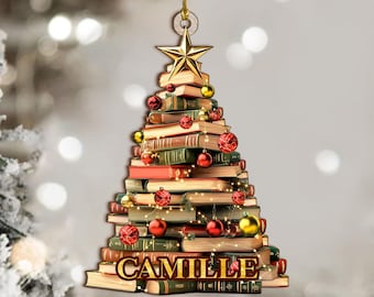 May include: A Christmas tree ornament shaped like a tree made of books. The books are stacked in a triangular shape, with a gold star on top. Red and gold ornaments are scattered throughout, and the name "CAMILLE" is at the base.