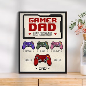 May include: A framed print with the words "GAMER DAD" in red pixelated font. Below, it reads "LIKE A NORMAL DAD ONLY MUCH COOLER." It features controller graphics with names: Megan, Liam, Olivia, and Dad. The frame is black.