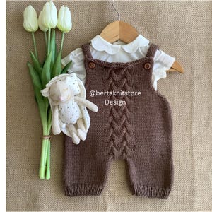 May include: A brown knitted baby romper with a cable knit design, paired with a white collared shirt. A stuffed bunny and a bouquet of white tulips are also in the image. The text "@bertaknitstore Design" is visible.