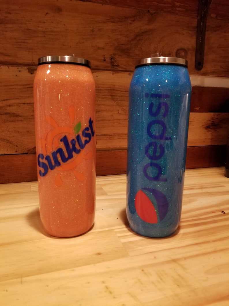 May include: Two glitter-covered stainless steel tumblers with lids. The tumbler on the left is orange with a Sunkist logo. The tumbler on the right is blue with a Pepsi logo.