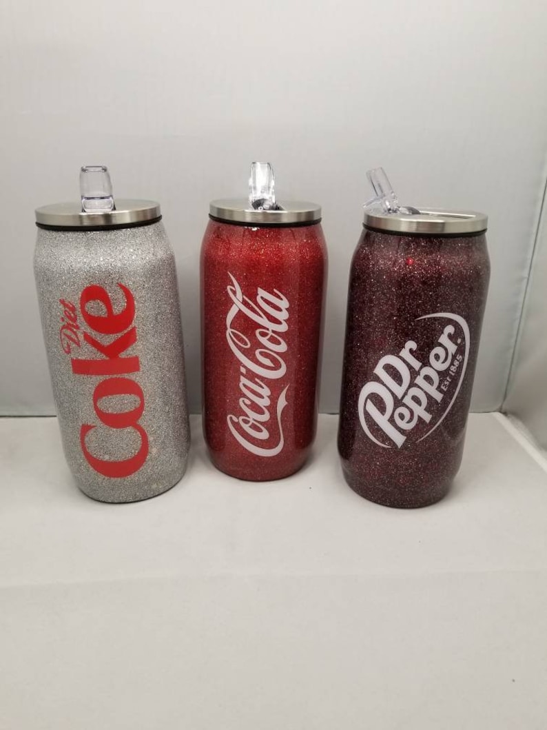 May include: Three stainless steel can-shaped tumblers with lids and straws. The tumblers are covered in glitter and feature the logos for Diet Coke, Coca-Cola, and Dr Pepper.
