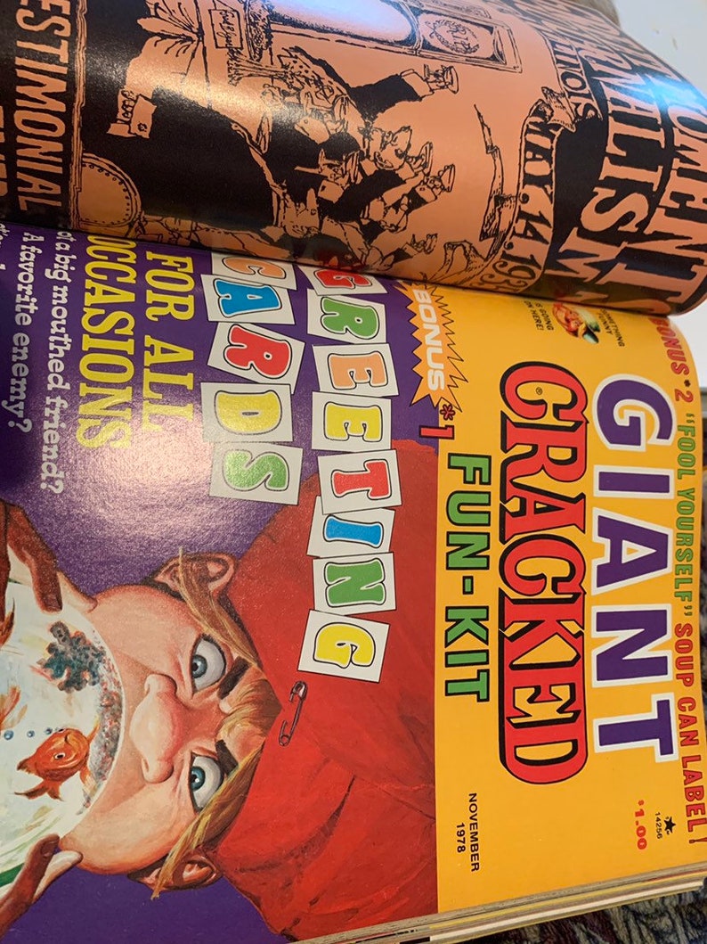 May include: A stack of vintage magazines with colorful covers. The top magazine has a peach-colored cover with black illustrations and text. The bottom magazine has a yellow cover with the text "GIANT CRACKED FUN-KIT" and a cartoon illustration.
