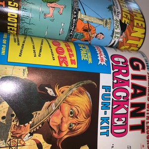May include: A stack of vintage magazines, with the top one featuring a cartoon illustration of a person with a quill pen and the title "GIANT CRACKED FUN-KIT". Other magazines show illustrations and text.