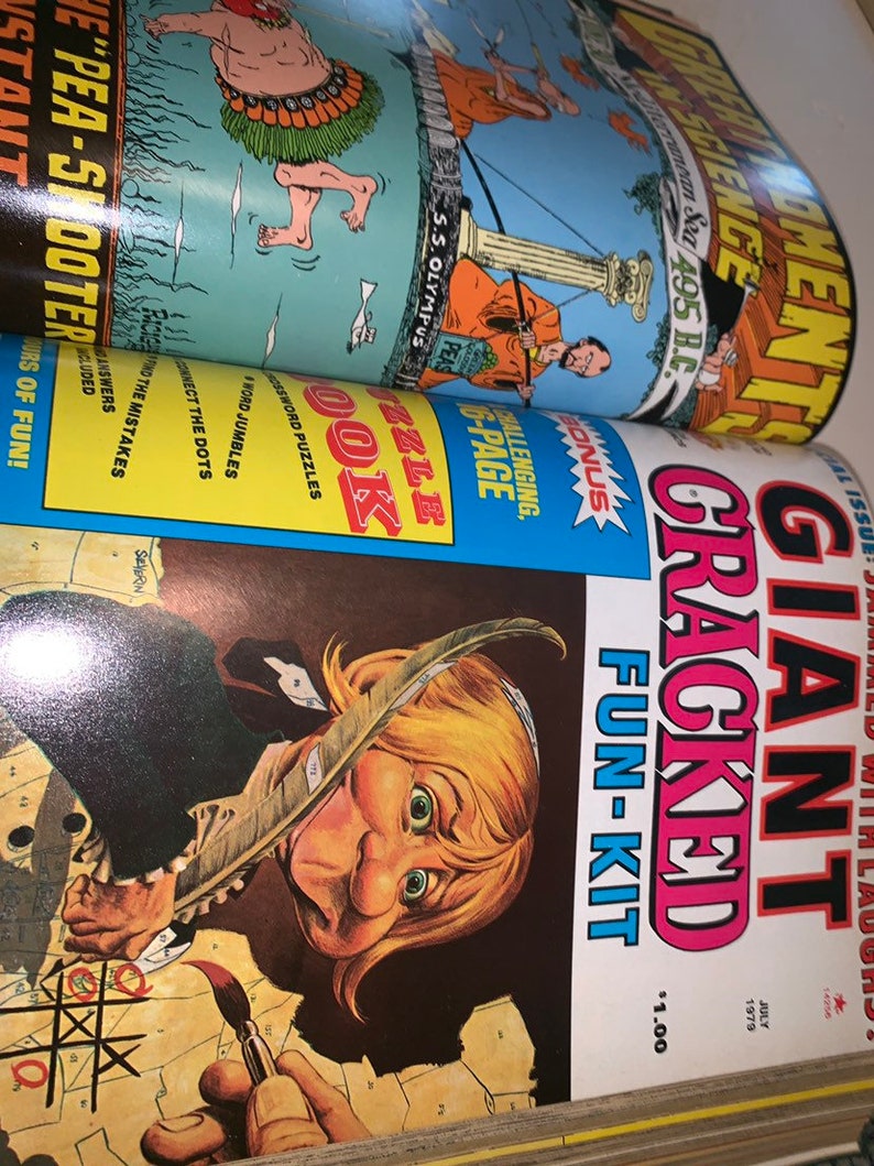 May include: A stack of vintage magazines, with the top one featuring a cartoon illustration of a person with a quill pen and the title "GIANT CRACKED FUN-KIT". Other magazines show illustrations and text.
