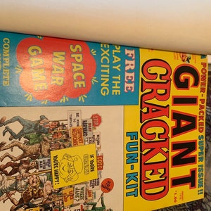 May include: Two vintage comic books. One features a blue cover with "Space War Game" and "Free Play the Exciting" text. The other has a yellow cover with "Giant Cracked Fun-Kit" and various cartoon illustrations. The comics are from January 1978.