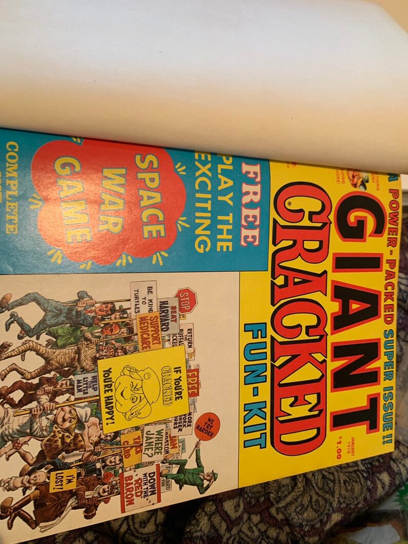 May include: Two vintage comic books. One features a blue cover with "Space War Game" and "Free Play the Exciting" text. The other has a yellow cover with "Giant Cracked Fun-Kit" and various cartoon illustrations. The comics are from January 1978.