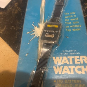 May include: A black and silver water-powered watch on a blue and white package. The package says "NEW HI-TECH PRODUCT" and "WORLDWIDE PATENT PENDING WATER WATCH". The watch has a digital display and the text "MEDANA H₂O WATCH&trade;". The package also says "The only watch in the world That runs on ordinary Tap water" and "NO BATTERY NEEDED RUNS ON TAP WATER SEA WATER BEER.ANY LIQU".