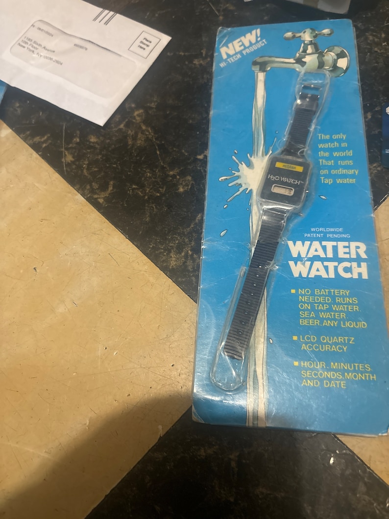 May include: A blue and white packaging card for a water-powered watch. The watch is black with a digital display and the text "H₂O WATCH" is printed on the face. The packaging card features a cartoon illustration of a faucet with water flowing from it. The text "NEW! HI-TECH PRODUCT" is printed at the top of the card. The text "WORLDWIDE PATENT PENDING WATER WATCH" is printed in large letters at the bottom of the card. The text "NO BATTERY NEEDED. RUNS ON TAP WATER SEA WATER BEER.ANY LIQUID" is printed in a smaller font below the large text. The text "LCD QUARTZ ACCURACY" is printed below the previous text. The text "HOUR. MINUTES. SECONDS.MONTH AND DATE" is printed at the bottom of the card.