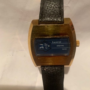 May include: A vintage Lucerne digital watch with a gold-tone case and a black leather band. The watch face is dark blue with white numerals and the word "DIGITAL" and "SWISS". The watch is a classic timepiece.