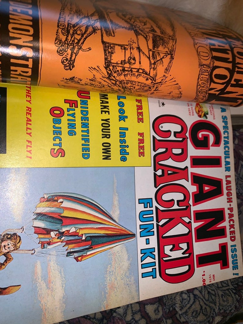 May include: A vintage magazine with the title "Giant Cracked Fun-Kit" in red and black, featuring a colorful parachute illustration. Other text includes "Unidentified Flying Objects" and "Demonstration".