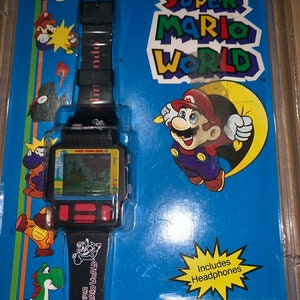 May include: A black and blue Nintendo Super Mario World watch with a game screen and buttons. The watch has a black band with the words "Super Mario World" printed on it. The watch is packaged in a blue and yellow box with a picture of Mario on it. The box also includes a pair of black headphones.