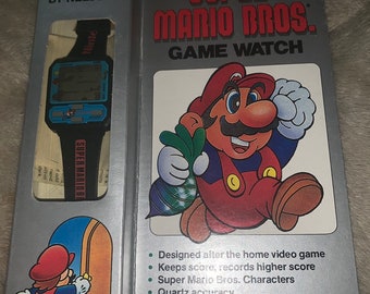 May include: A Nintendo Super Mario Bros. Game Watch, featuring a red and blue box with a cartoon image of Mario holding a power-up. The box includes the text "Super Mario Bros. Game Watch" and "Official Nintendo Licensed Product".