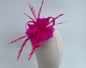 May include: A bright pink feather and flower hair clip. The clip is on a white mannequin head.
