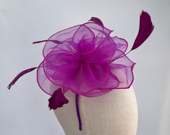 May include: A magenta fabric flower headband with feathers. The headband is on a white mannequin head.