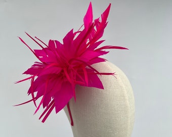 May include: A bright pink feather headband with a large, fluffy feather design. The headband is on a white mannequin head.