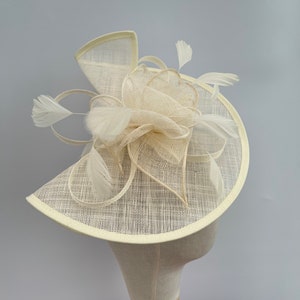 May include: A white, circular, wide-brimmed hat with a large, white, feathered flower accent.