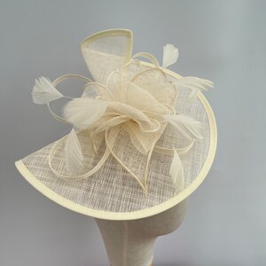 May include: A cream-colored hat with a large, floppy brim and a delicate, white feather embellishment.