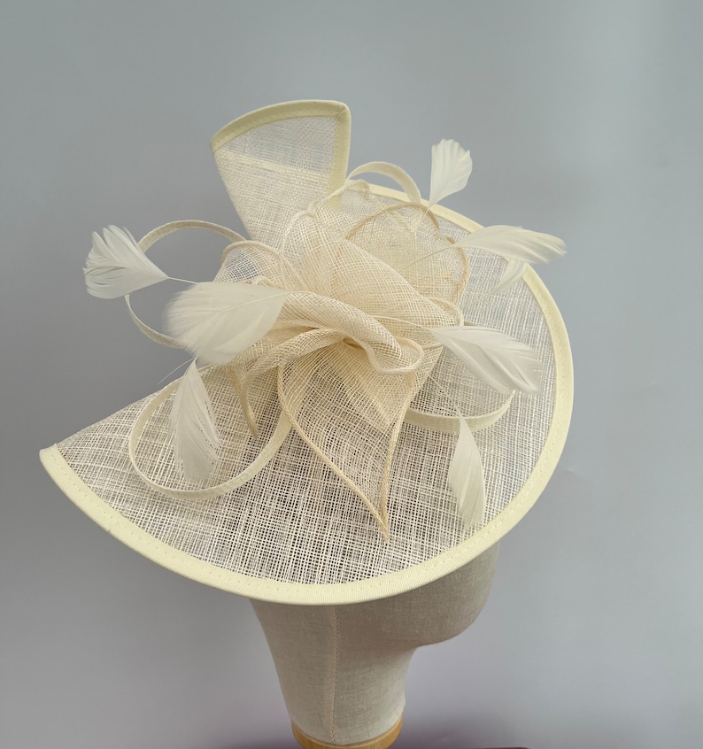 May include: A cream-colored hat with a large, floppy brim and a delicate, white feather embellishment.