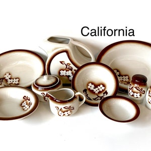May include: A set of brown and white ceramic dishes with a floral design. The set includes a pitcher, a large bowl, four smaller bowls, a creamer, a sugar bowl, and two salt and pepper shakers. The dishes are all decorated with a brown rim and a white floral design.
